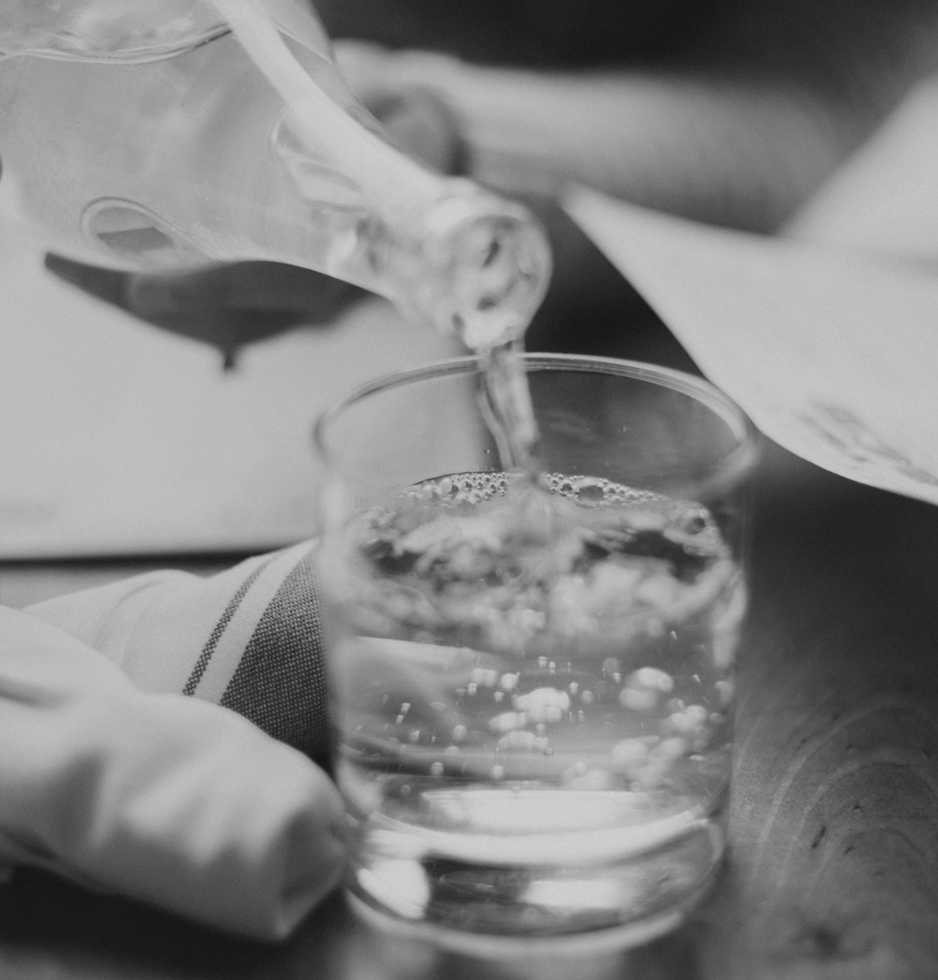 Photograph of someone pouring water from a bottle into a glass (restaurant setting)