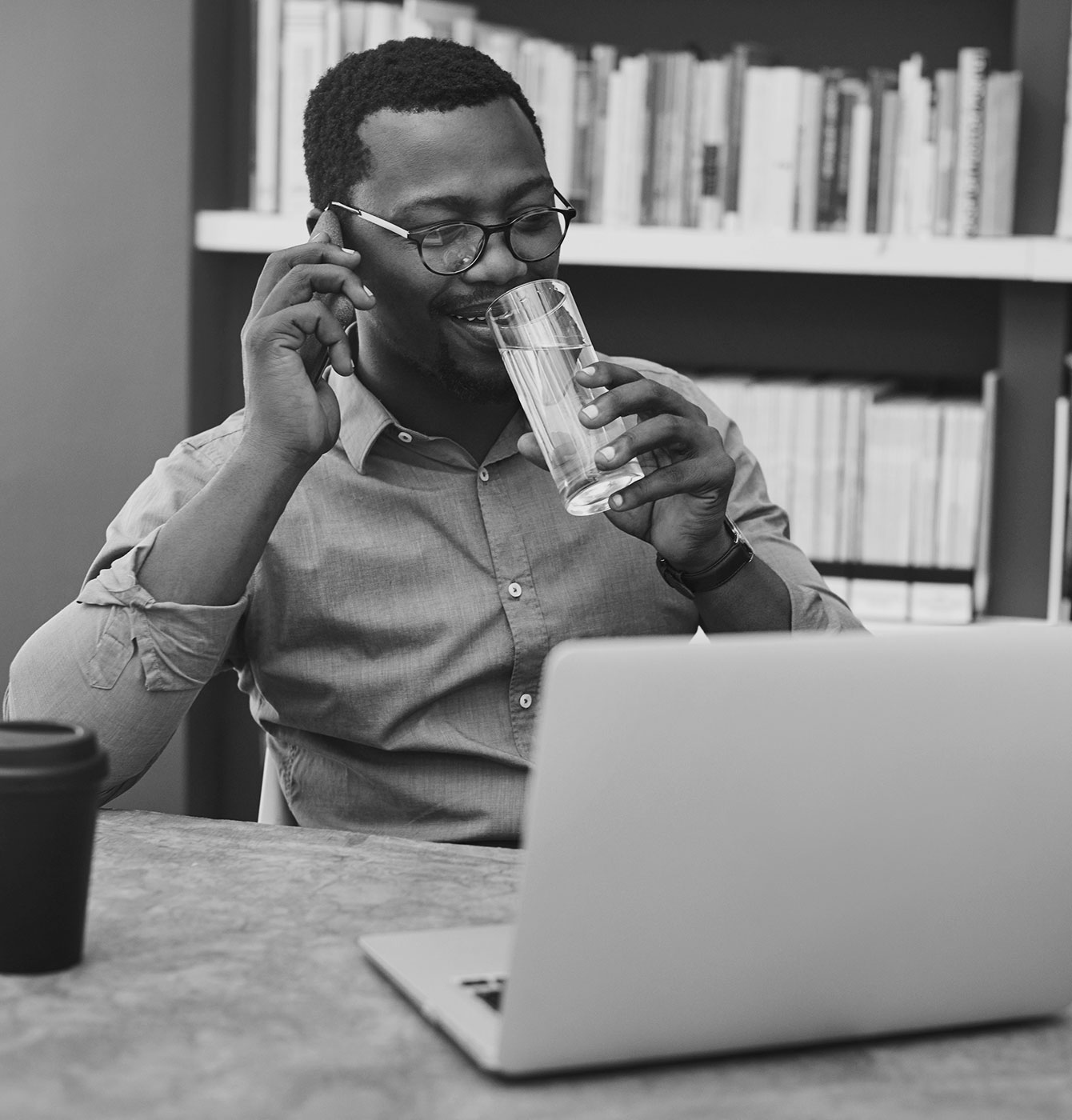 Photograph of a man talking on the phone while drinking from a glass of water