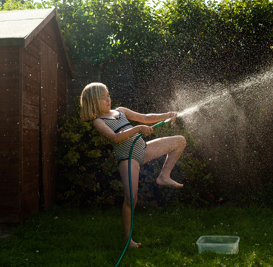 Photograph of a young girl playing with a garden hose (spaying water).